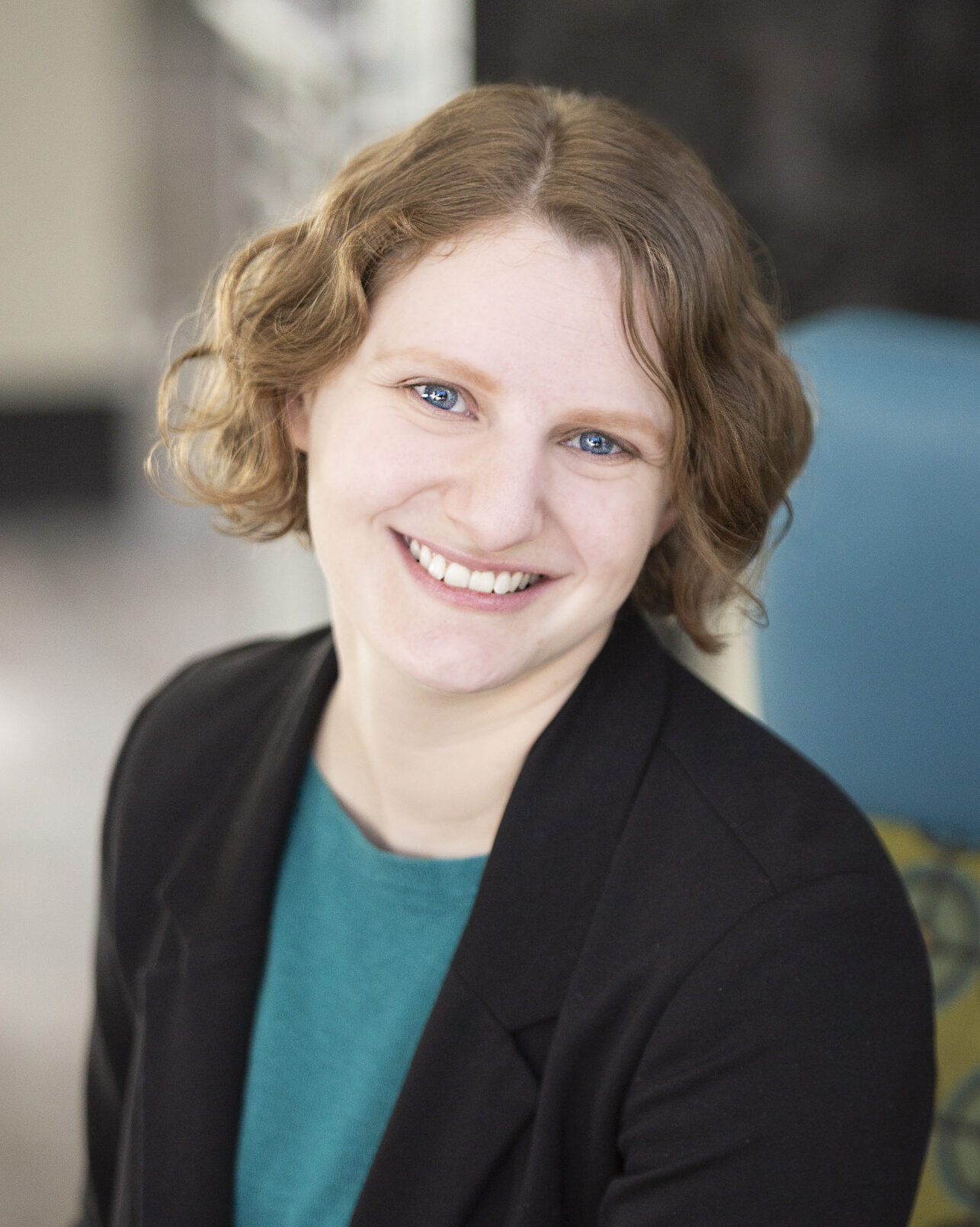 Headshot of woman smiling, wearing a teal sweard black blazer.